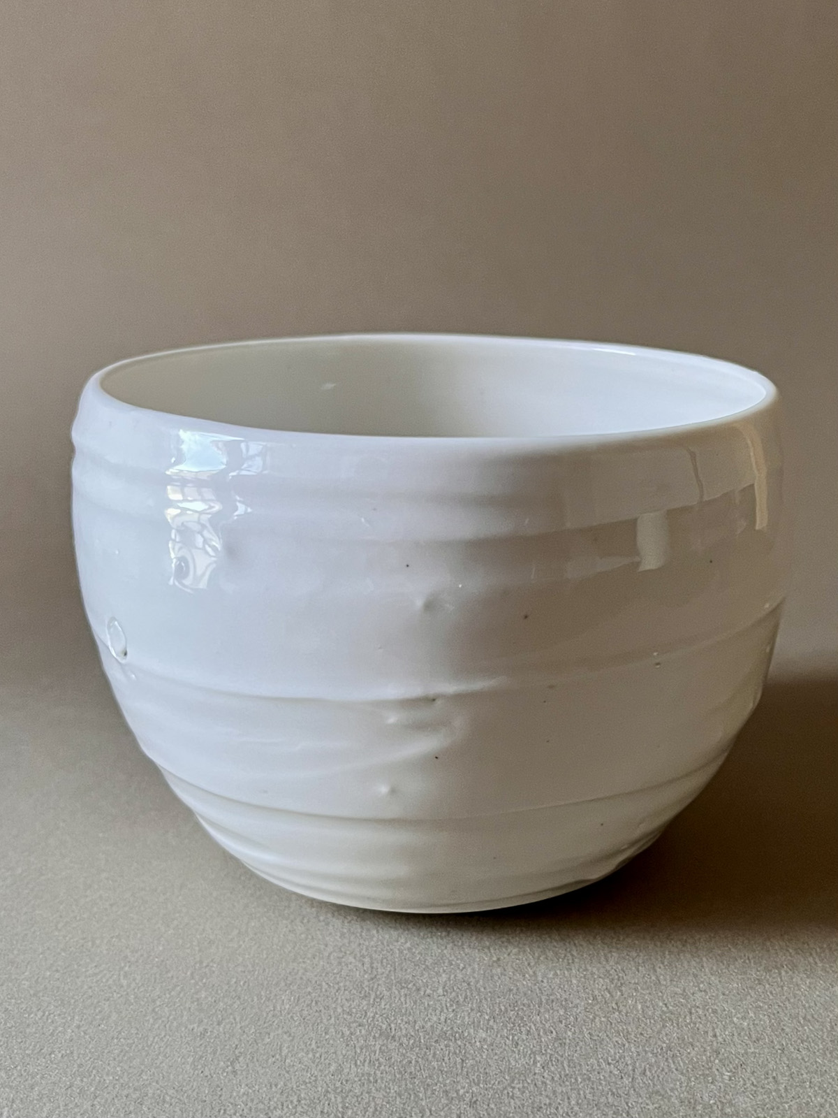 Bol Purete en porcelaine blanche brillante aux parois légèrement striées, vue de face sur fond beige