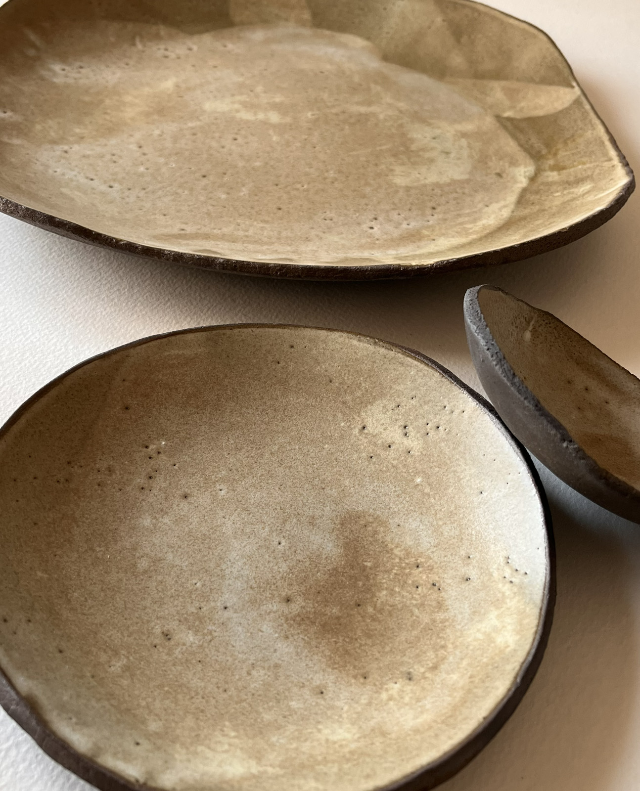 Assiettes et coupelle en grès brun à l'émail beige nuageux, formes libres, vues de dessus