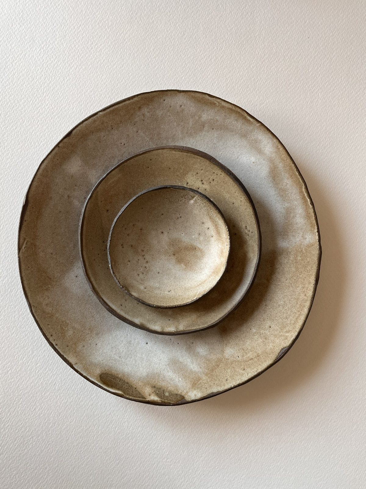 Assiette, petite assiette et coupelle en grès brun émaillé beige empilées, vues de dessus