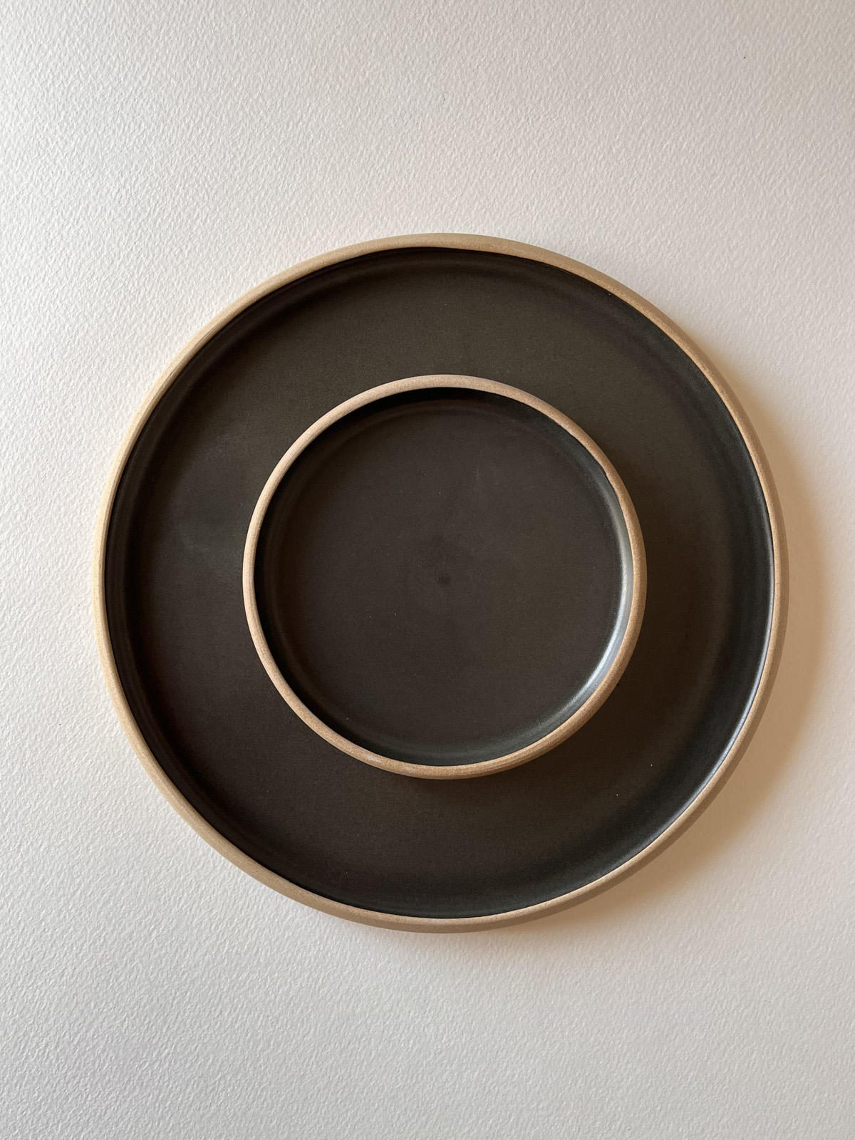 Deux assiettes rondes en grès émaillé noir mat au bord laissé brut, emboîtées, vues de dessus