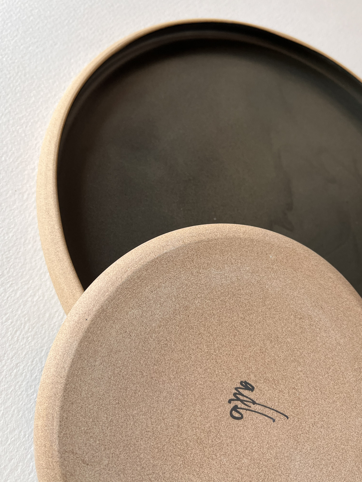 Assiette en grès noir mat retournée montrant son dessous en grès brut signé adb, seconde assiette dessous