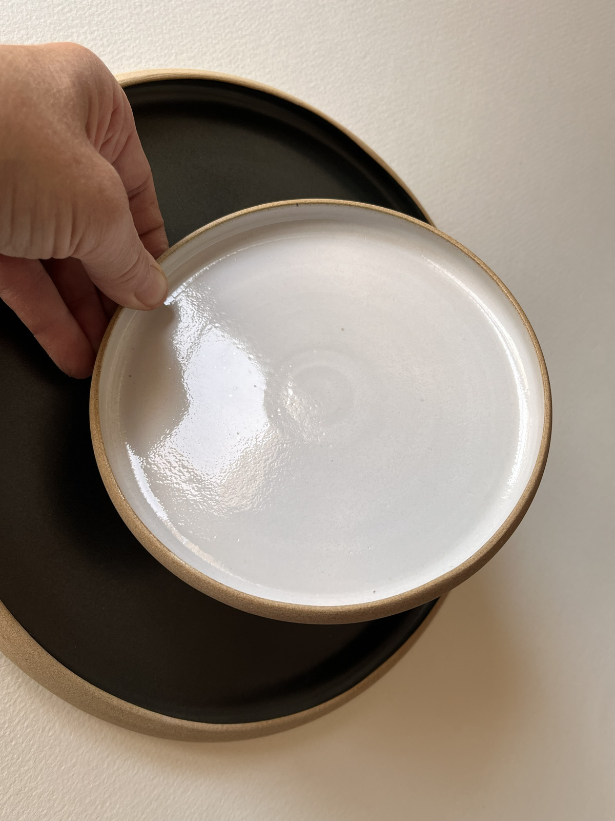 Main tenant une petite assiette blanche brillante au-dessus d'une grande assiette noire mate à bord brut