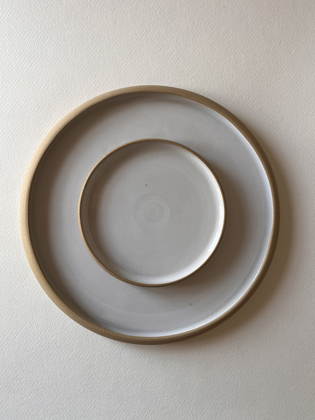 Deux assiettes rondes émaillées blanc à bord de grès brut, emboîtées, vues de dessus