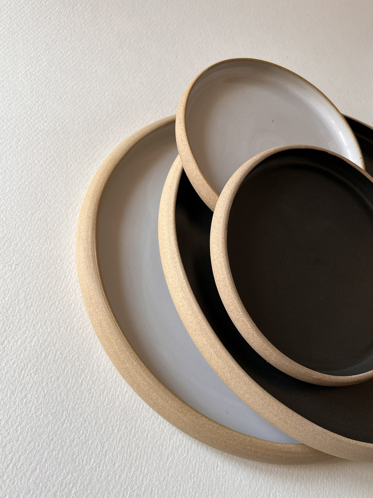 Pile d'assiettes rondes émaillées blanc et noir mat à bord de grès brut, de plusieurs tailles