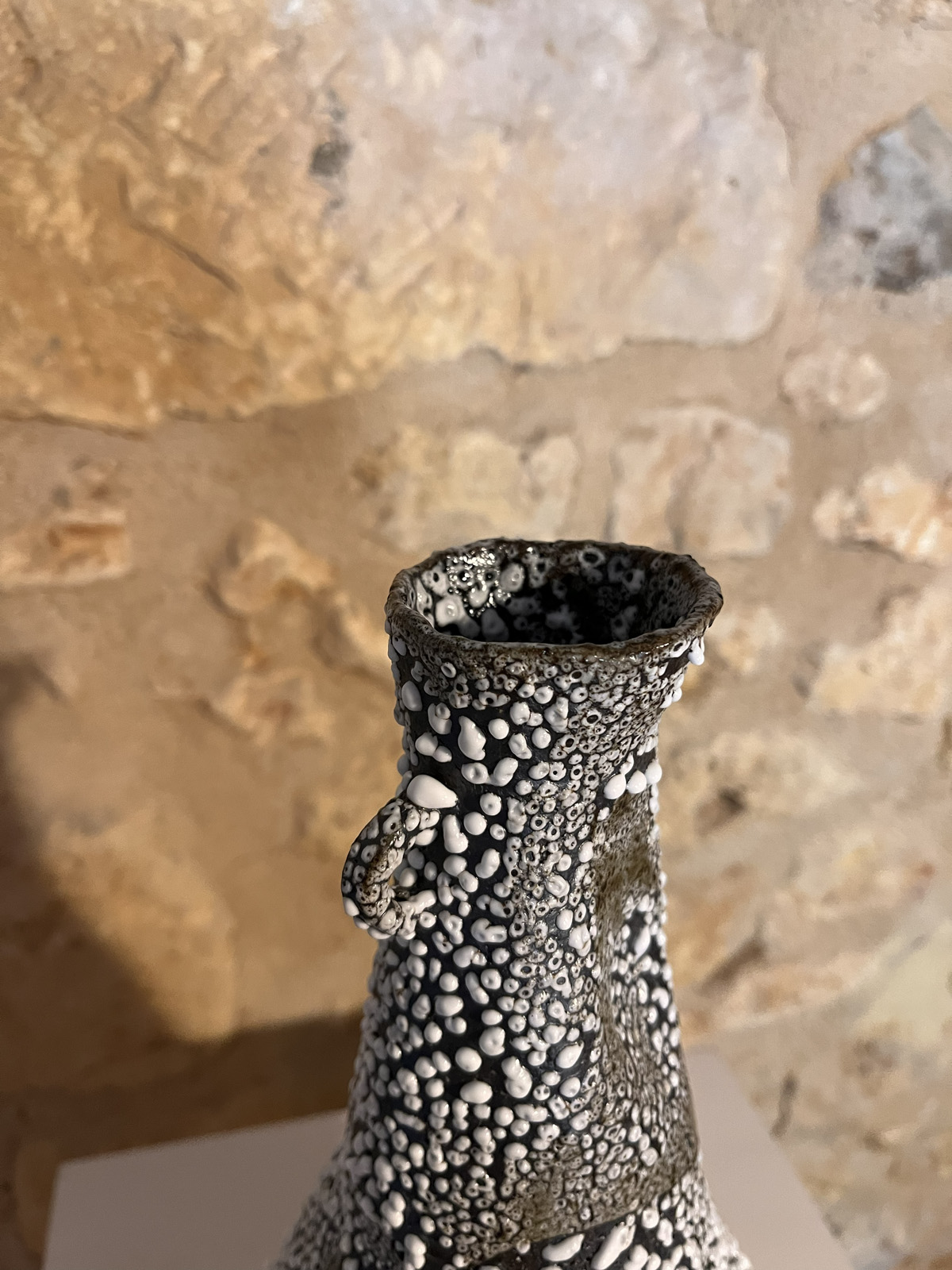 Gros plan sur le col et l'émail blanc rétracté en billes d'un vase Winter exposé devant un mur de pierre