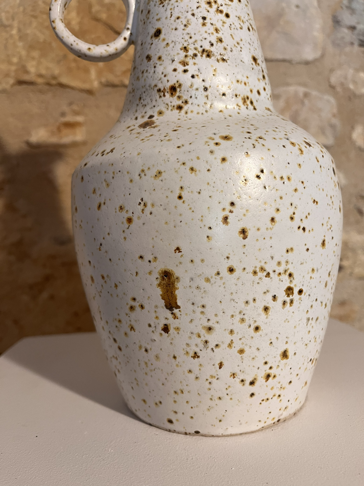 Gros plan sur la panse en grès blanc moucheté de brun d'un vase à anneaux, anneau visible en haut