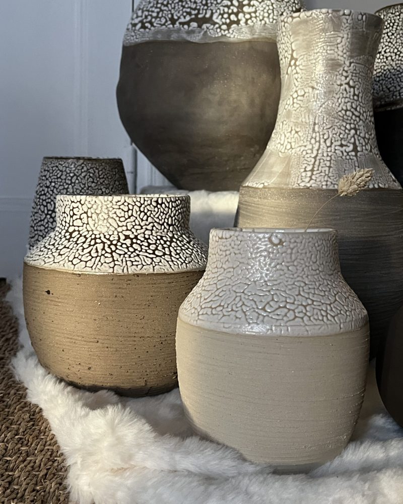 Vases Winter beige et brun sur peau blanche Vases Winter en grès beige et brun aux cols émaillés blanc rétracté, posés sur une peau blanche, vue rapprochée