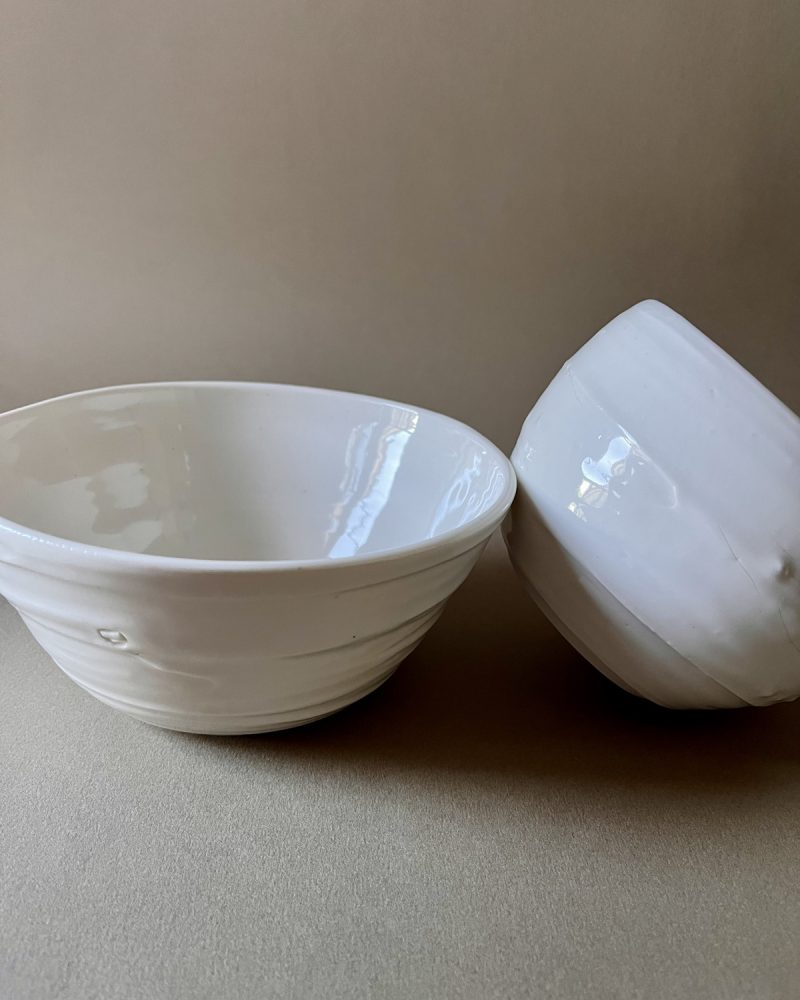 Deux bols Purete en porcelaine blanche brillante, l'un appuyé contre l'autre, sur fond beige