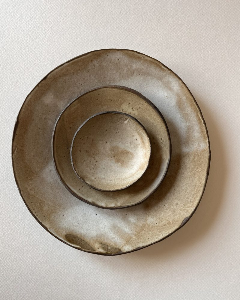 Assiettes et coupelle brun et beige empilées, vue de dessus Assiette, petite assiette et coupelle en grès brun émaillé beige empilées, vues de dessus