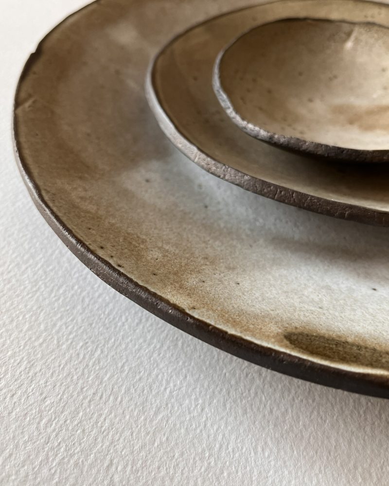 Assiettes brun et beige, bords en gros plan Gros plan sur les bords irréguliers d'assiettes en grès brun à l'émail beige nuageux empilées