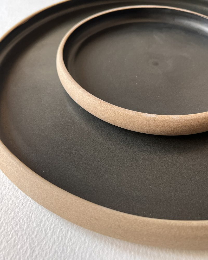 Vue rapprochée de deux assiettes rondes en grès noir mat à bord brut, l'une posée sur l'autre