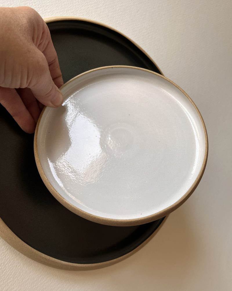 Main tenant une petite assiette blanche brillante au-dessus d'une grande assiette noire mate à bord brut