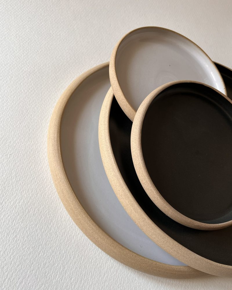 Pile d'assiettes rondes émaillées blanc et noir mat à bord de grès brut, de plusieurs tailles