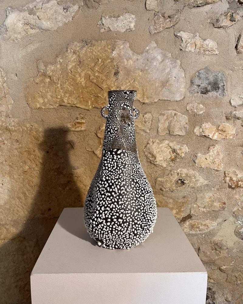 Vase Winter entièrement couvert d'émail blanc rétracté sur grès noir, sur socle devant un mur de pierre