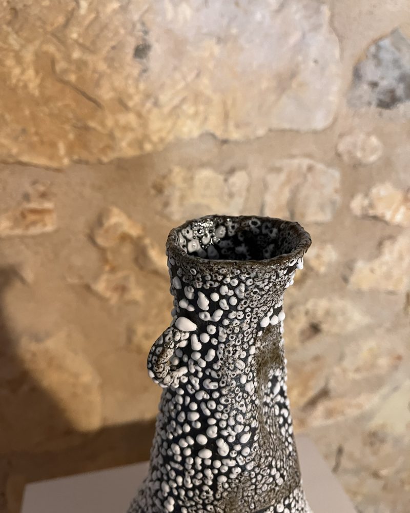 Gros plan sur le col et l'émail blanc rétracté en billes d'un vase Winter exposé devant un mur de pierre