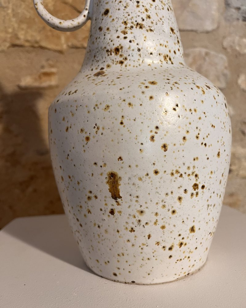 Gros plan sur la panse en grès blanc moucheté de brun d'un vase à anneaux, anneau visible en haut